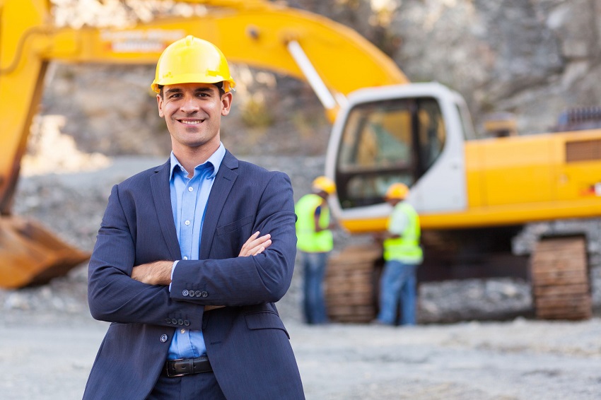 man wearing hard hat with his arms crossed in from of excavator
